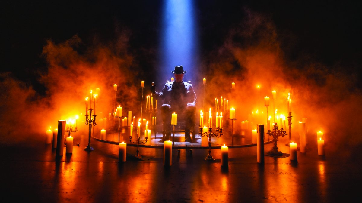 Mustahattuinen mies sumun ja kynttilöiden keskellä