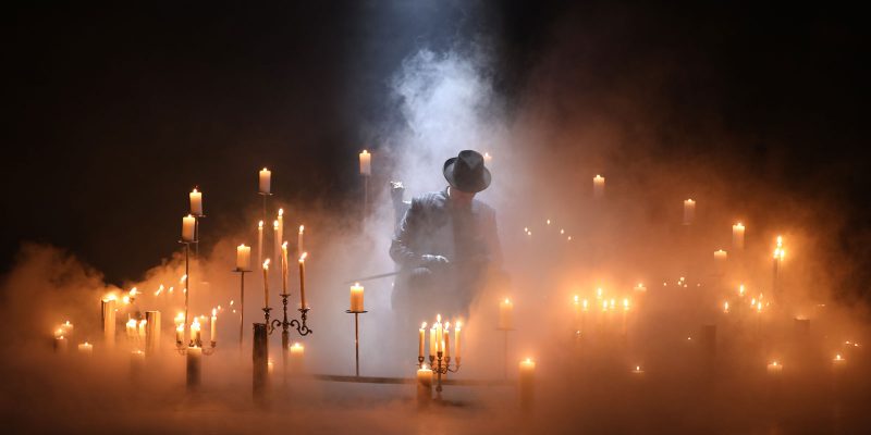 Mustahattuinen mies sumun ja kynttilöiden keskellä